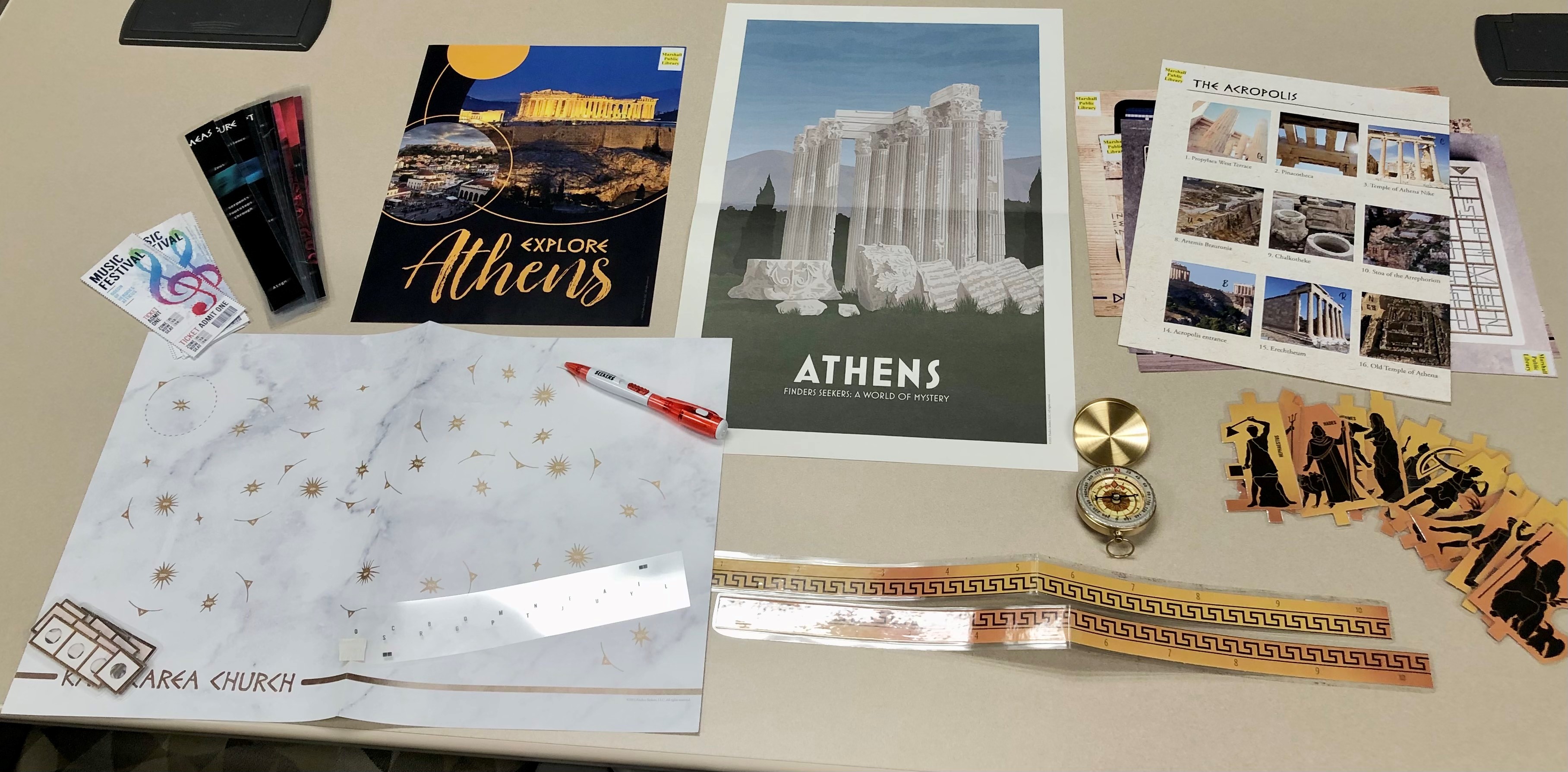 A photo of the Finders seekers: Athens kit. Photo includes various fliers and posters of Athens, music festival tickets, a compass, puzzles, and maps.