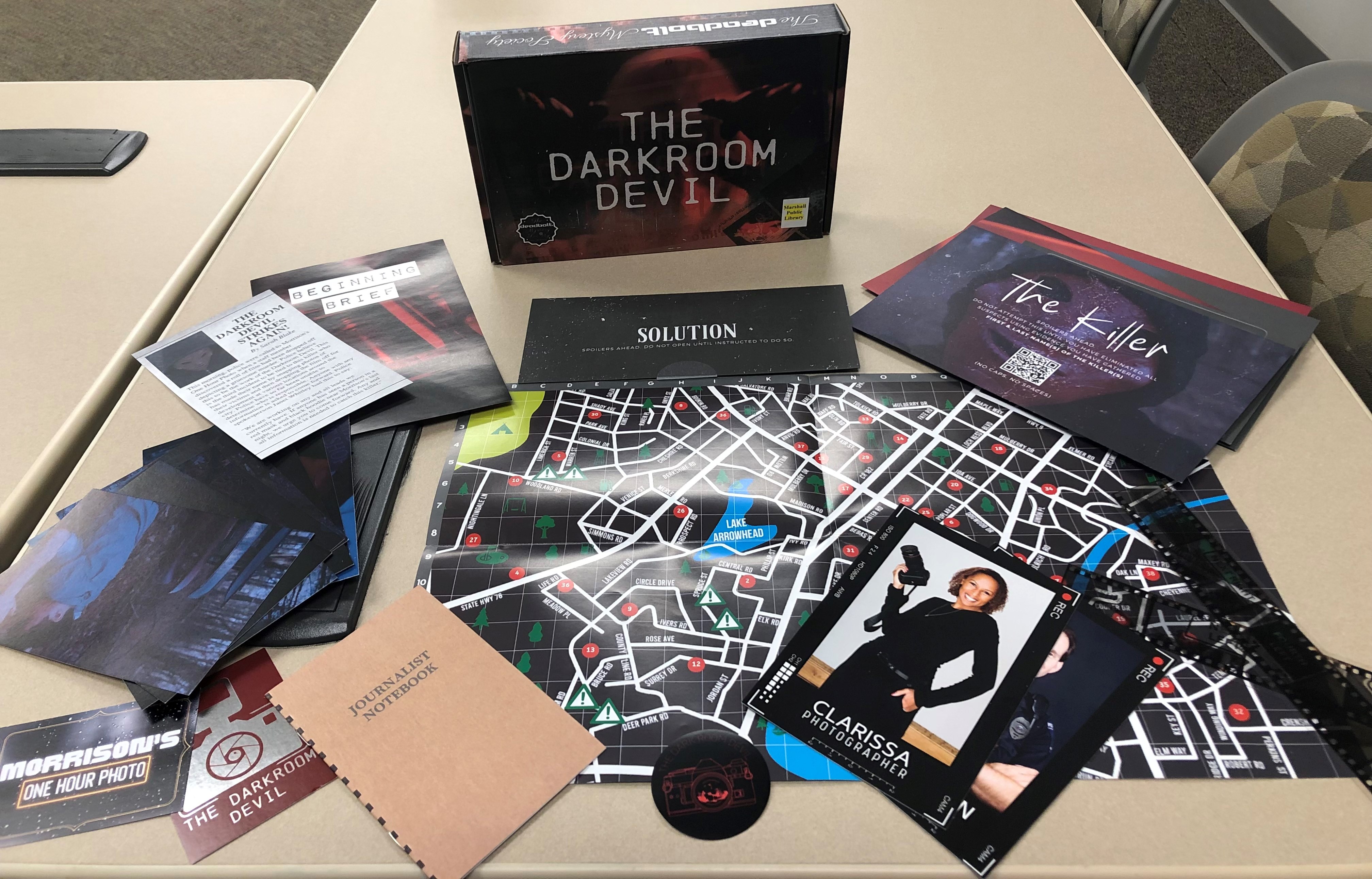 A photograph of the Darkroom Devil kit from The Deadbolt Mystery Society. The photo shows a map, photographs, and various clues.