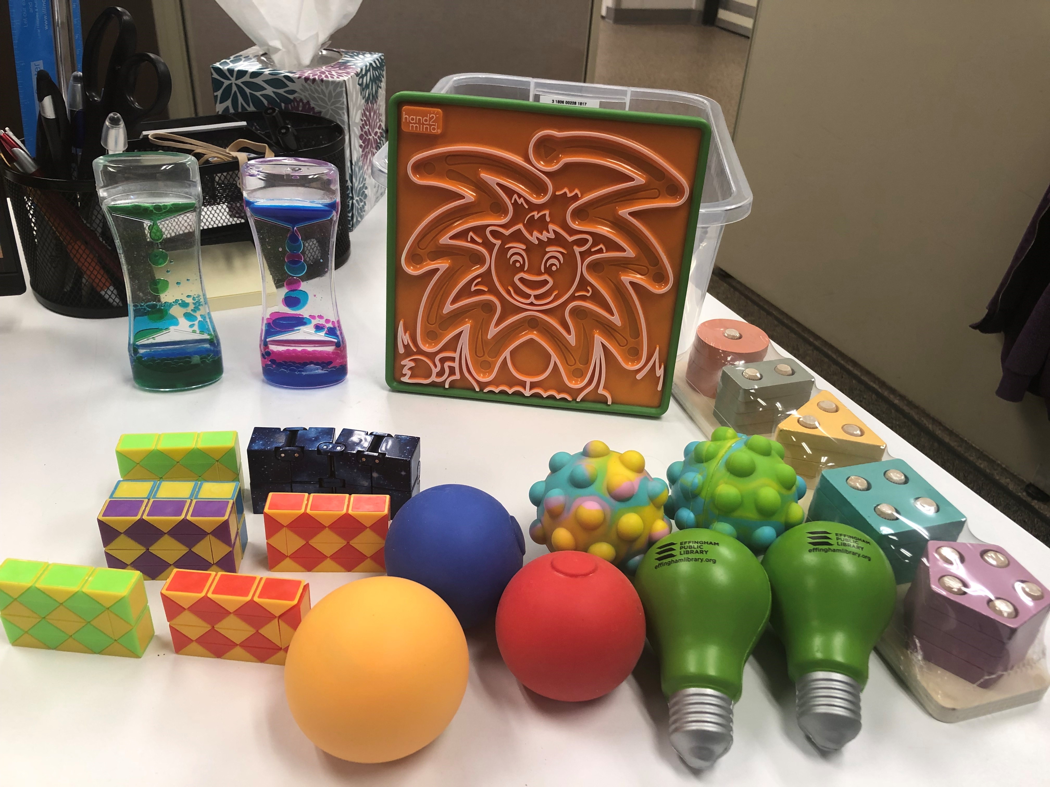 Photo of a fidget kit consisting of stress balls, liquid hour glasses, a memory puzzle, and other tactile objects.