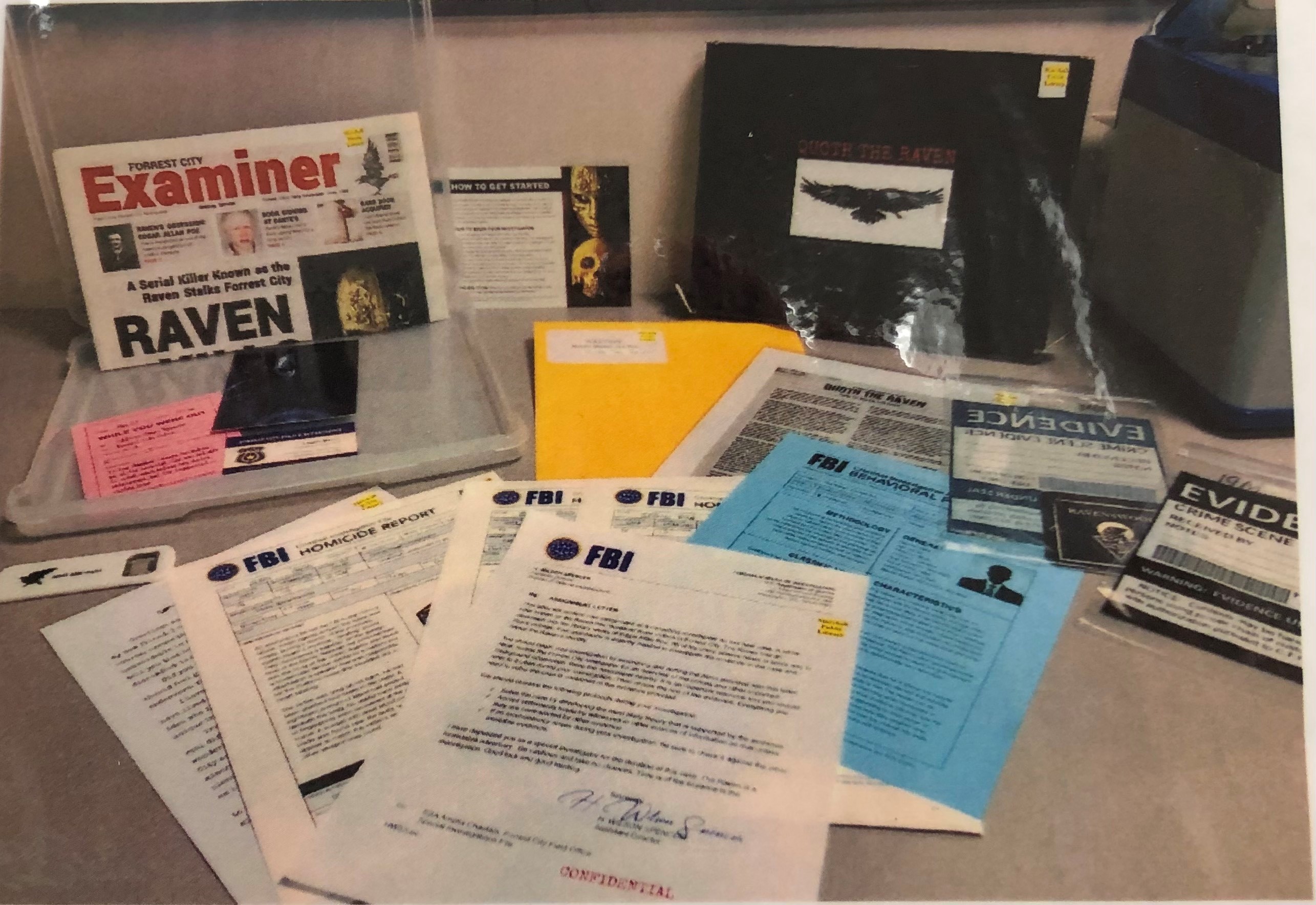 A photograph of the Quoth the Raven kit from The Mysteries Experiences Company. Photo shows a variety of clues like FBI documents, newspapers, bagged evidence, and a magnifier.