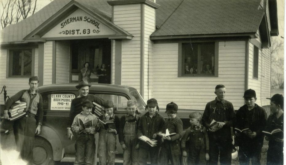 a group of boys posing with their newly acquired books alongside the Clark County Bookmobile in front of the Sherman School building